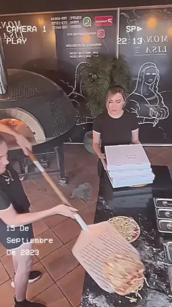 Two pizza restaurant employees have trouble picking up the pizza and getting it into the o