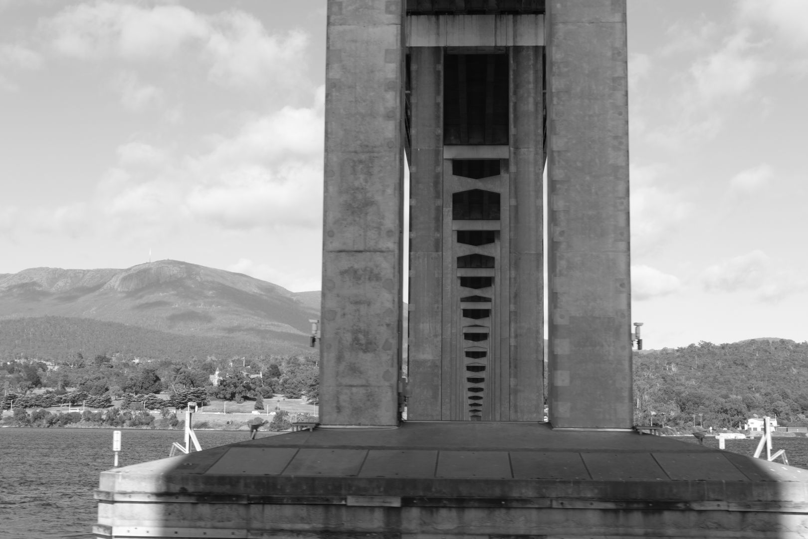 A black and white photo looking under a large concrete bridge through the support pillars