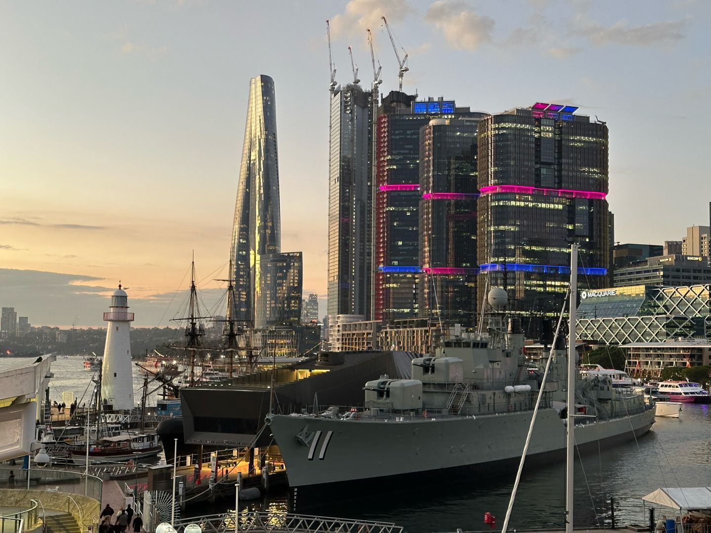 Ships and a lighthouse in the foreground, the skyscrapers of Barangaroo in the distance, sunset sky but looking north east