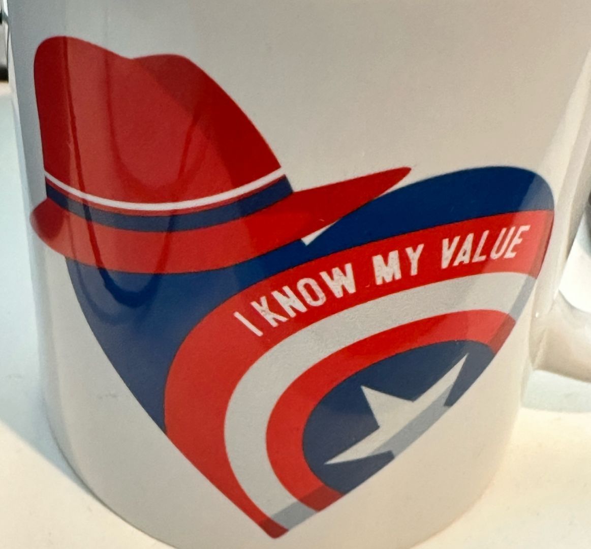 A coffee/tea mug with a Marvel Universe Agent Carter logo with “I know my value” written in the logo. The logo has a heart with a Captain America shield and a red hat depicting Agent Carter’s hat