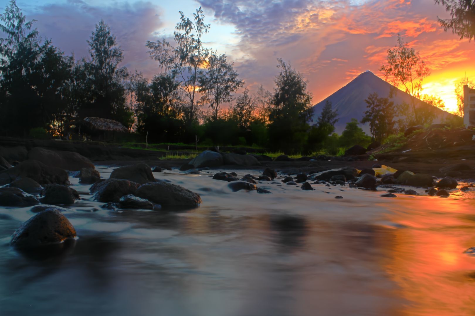 A perfect-cone volcano stands on the rights hand side of the photo. On the foreground is the sea. It is almost dusk