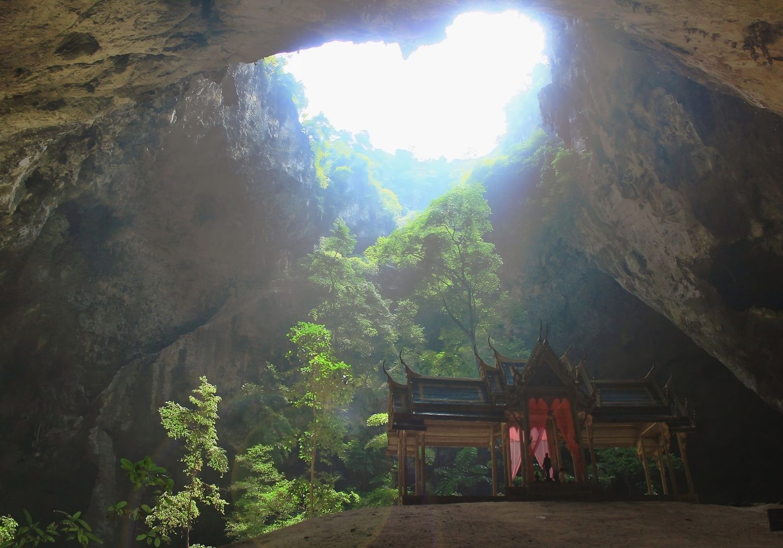 A Buddhist temple is lit by the sunlight peeking through a hole in the ceiling of a cave